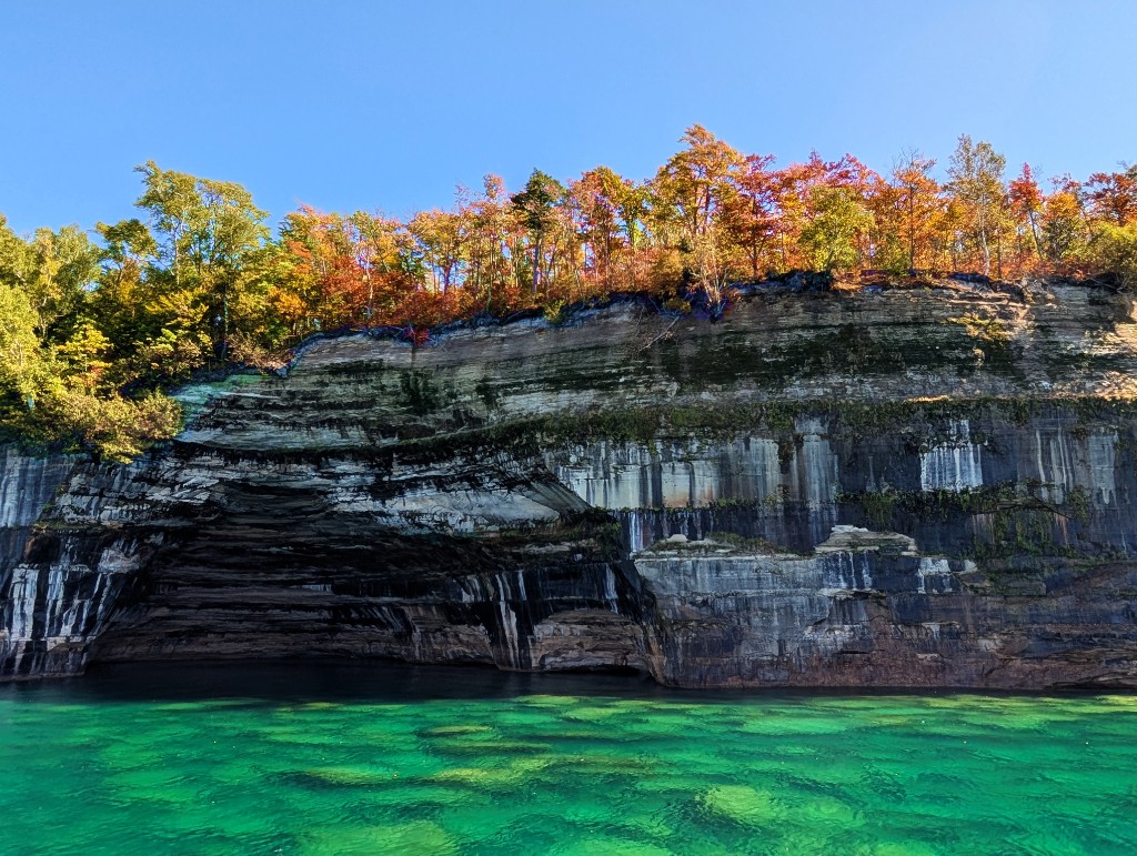 Sandstone cliffs and autumn trees above turquoise water at Pictured Rocks, Michigan
